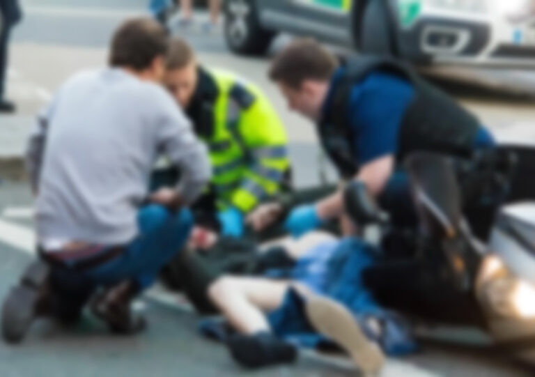 Imagen en la que aparecen varias personas socorriendo a una persona tendida sobre el suelo tras tener un accidente de tráfico