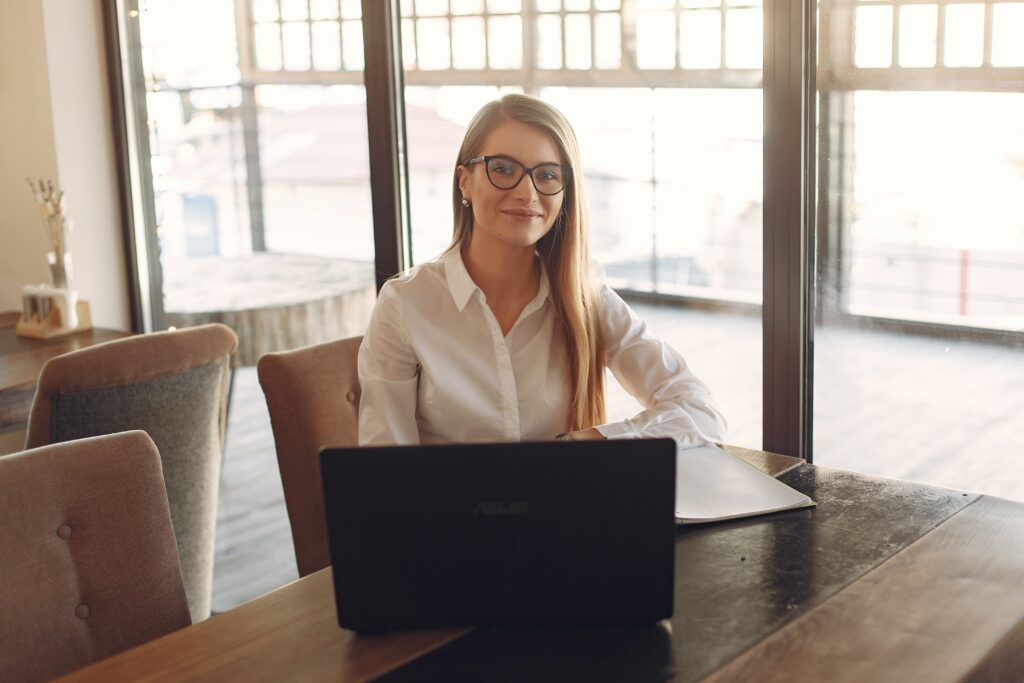 En la imagen aparece una mujer sentada frente a la pantalla de su ordenador portátil, mirando a la cámara
