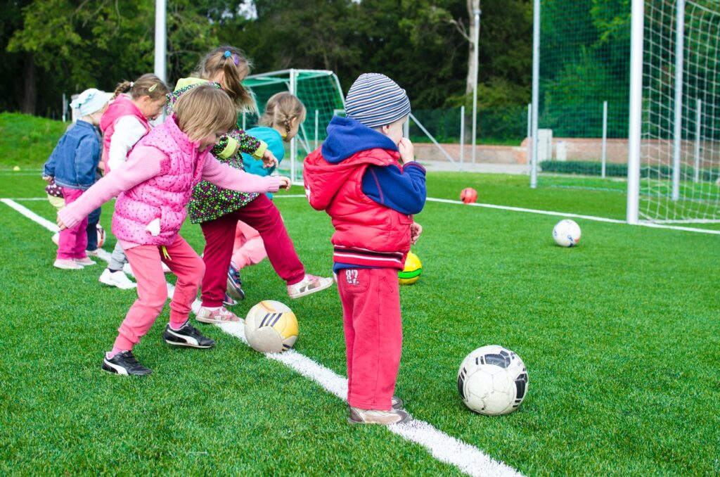 En la imagen aparecen varios niños jugando con balones en un campo de fútbol de hierba