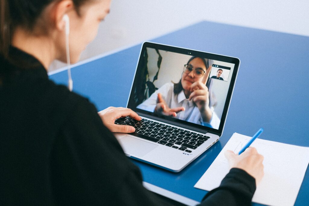Una mujer sentada frente a un ordenador portátil toma notas mientras realiza una reunión online con sus compañeros de trabajo