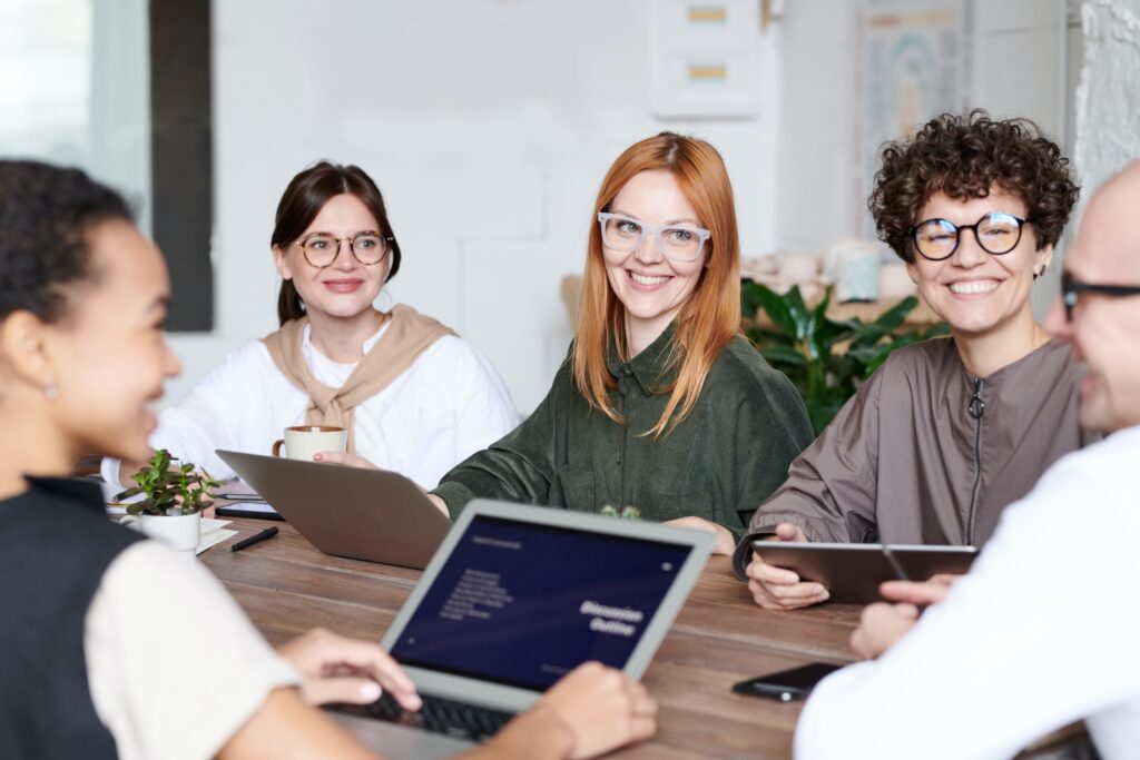 En la imagen aparece un grupo de personas trabajando alrededor de una amplia mesa, rodeado de ordenadores y de dispositivos móviles. Ambiente distendido en una oficina