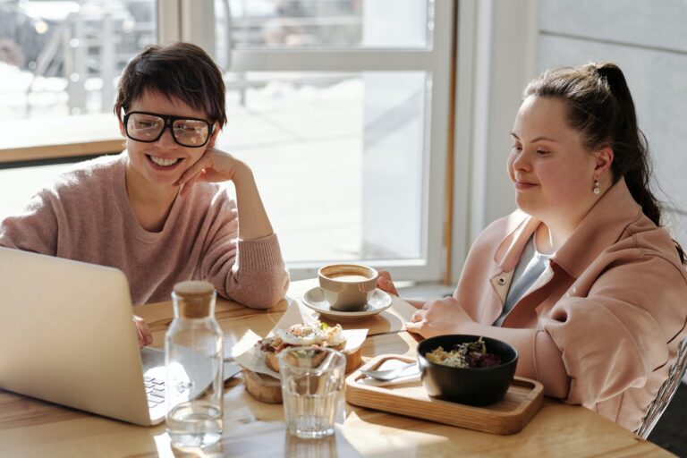 En la imagen aparecen dos mujeres desayunando y mirando mientras sonríen una pantalla de ordenador