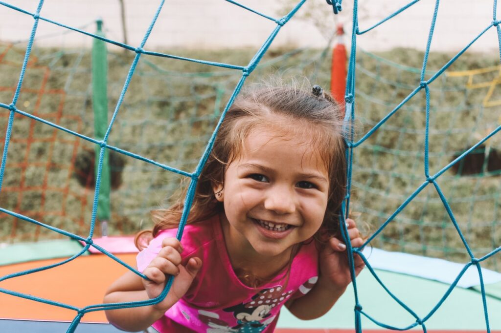 En la imagen aparece una niña sonriendo mientras juega en un parque