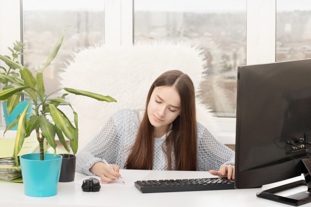 Imagen en la que aparece una mujer sentada frente a una pantalla de ordenador tomando nota mientras estudia el curso en modalidad Aula Virtual "Chino básico en actividades de venta y turismo"